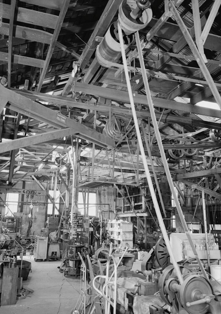 MACHINE SHOP NORTH/NORTHEAST INCLUDING OVERHEAD LINE SHAFTING. MOSTLY BELT DRIVEN WITH ONE ROPE DRIVEN LATHE IN MIDDLE GROUND. POWER COMES FROM KNIGHT TURBINE ON FAR WALL. This image is available from the United States Library of Congress